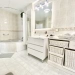 Baño contemporáneo con bañera redonda, lavabo blanco y almacenamiento en cestas de mimbre, decorado con azulejos claros.